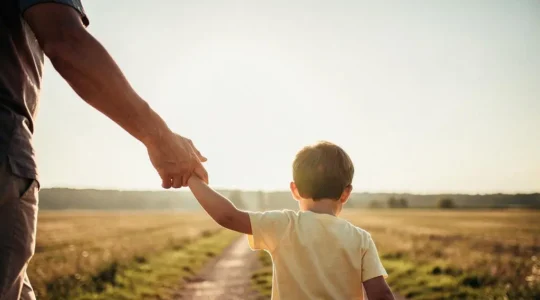 Un parent guidant la main d'un enfant sur un chemin ensoleille, symbole de la protection financiere transmise pour son avenir